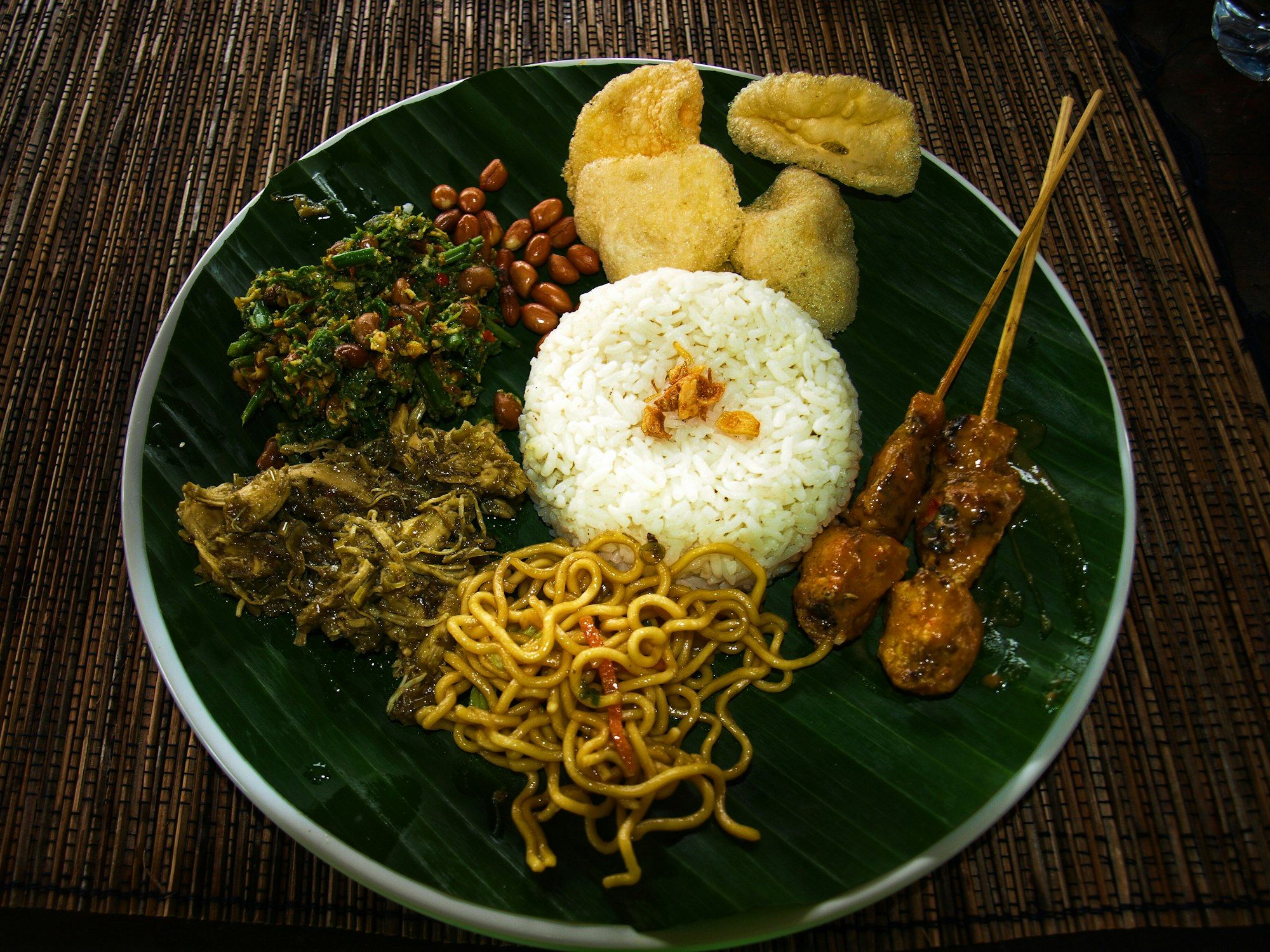Nasi campur di atas daun pisang: lawar sayur berkacang, ayam suwir bumbu hijau, mi goreng, dan sate lilit